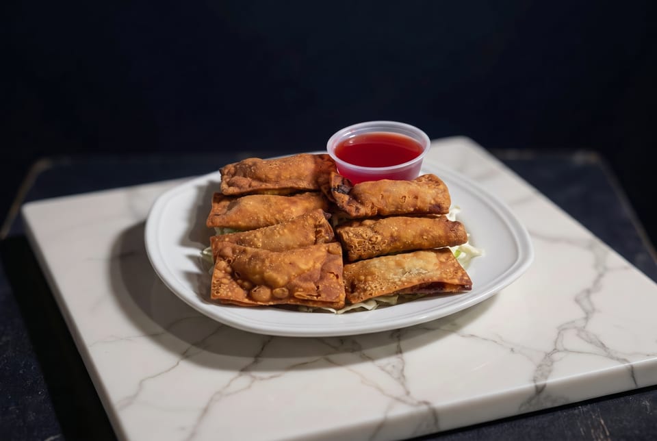 Crispy fried spring rolls and wontons on a white plate with a side of red dipping sauce.