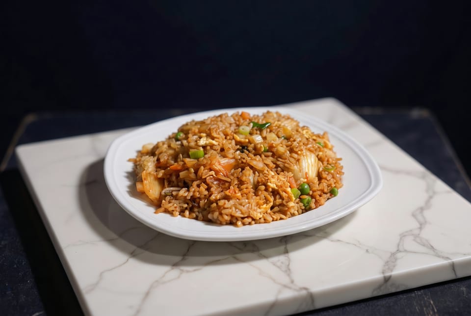 A white plate of kimchi fried rice with peas and green onions on a marble slab.